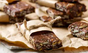 Domowe batony proteinowe z nasionami i bakaliami, zawinięte w papier i przewiązane sznurkiem. Idealne, gdy zastanawiasz się, jakie batony proteinowe wybrać.