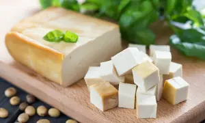Wegański ser z soi, pokrojony w kostkę i w bloku, leży na desce. Obok leżą ziarna soi.