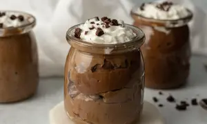 Jak zrobić pudding proteinowy: czekoladowy deser w słoiczku, udekorowany bitą śmietaną i kawałkami czekolady.
