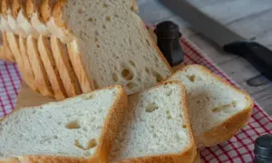 Pokrojony domowy chleb bezglutenowy na desce, obok solniczka i nóż.