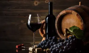 Kieliszek czerwonego wina, butelka, beczka i winogrona. Zastanawiasz się, czemu wino nie jest wegańskie? Czasem używa się produktów odzwierzęcych do klarowania.