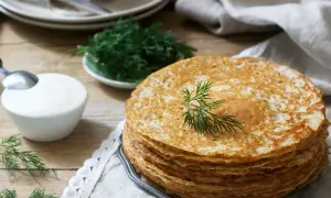 Stos naleśników bezglutenowych, ozdobiony gałązką koperku, obok miseczki śmietany i świeżego koperku. Idealne na śniadanie.