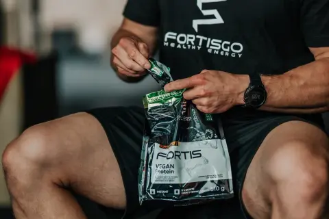 Mężczyzna otwiera opakowanie odżywki białkowej Fortis Vegan Protein. Zastanawiasz się, ile kalorii ma shake proteinowy?