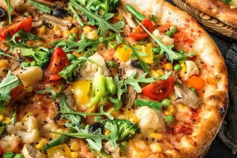 Pizza wegetariańska jakie dodatki? Brokuły, pomidorki, kukurydza, papryka, oliwki, pieczarki i rukola tworzą barwną kompozycję.
