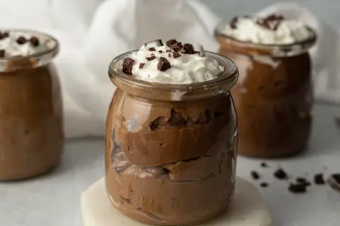 Jak zrobić pudding proteinowy: czekoladowy deser w słoiczku, udekorowany bitą śmietaną i kawałkami czekolady.