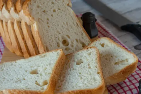 Pokrojony domowy chleb bezglutenowy na desce, obok solniczka i nóż.