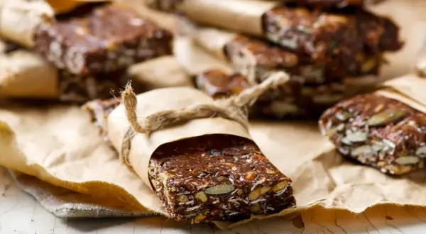 Domowe batony proteinowe z nasionami i bakaliami, zawinięte w papier i przewiązane sznurkiem. Idealne, gdy zastanawiasz się, jakie batony proteinowe wybrać.
