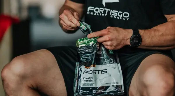 Mężczyzna otwiera opakowanie odżywki białkowej Fortis Vegan Protein. Zastanawiasz się, ile kalorii ma shake proteinowy?