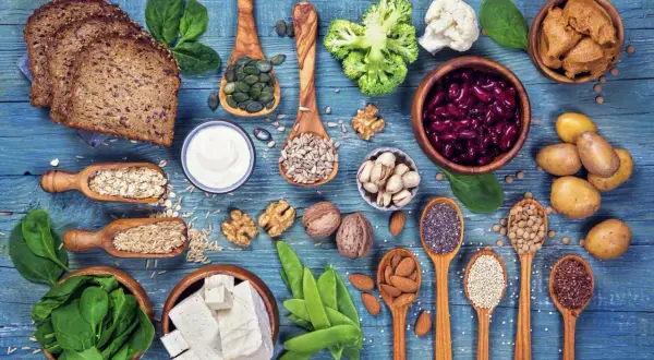 Różnorodne produkty roślinne bogate w białko: pieczywo, warzywa, nasiona, orzechy, tofu, fasola.