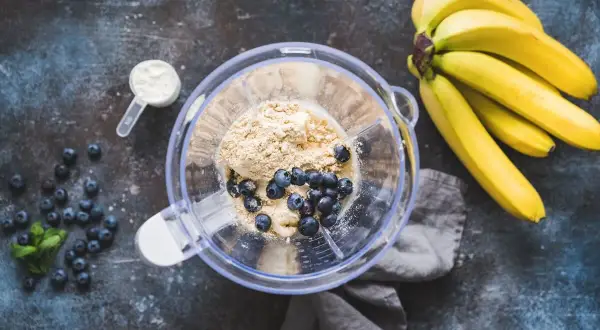 Jak zrobić shake proteinowy: banany, borówki, odżywka białkowa i mleko w blenderze.