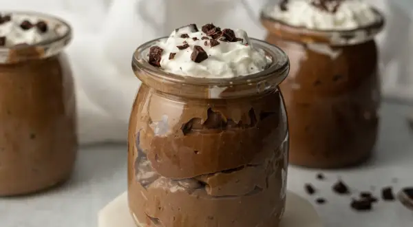 Jak zrobić pudding proteinowy: czekoladowy deser w słoiczku, udekorowany bitą śmietaną i kawałkami czekolady.