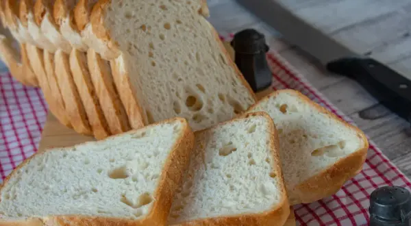 Pokrojony domowy chleb bezglutenowy na desce, obok solniczka i nóż.