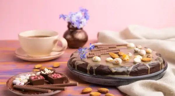 Czekoladowy tort z migdałami i słodkimi kuleczkami, idealny przepis na zdrowy deser. Obok filiżanka kawy i czekoladki.