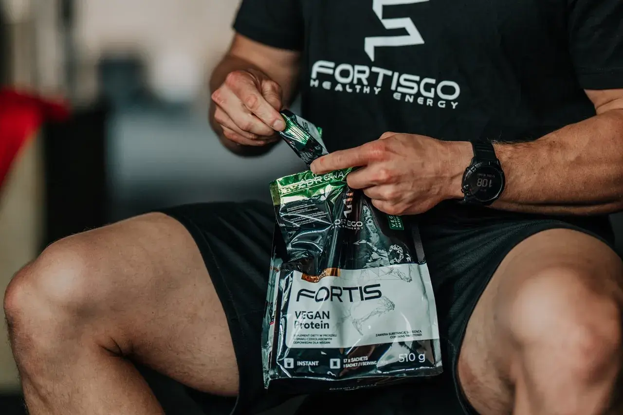 Mężczyzna otwiera opakowanie odżywki białkowej Fortis Vegan Protein. Zastanawiasz się, ile kalorii ma shake proteinowy?