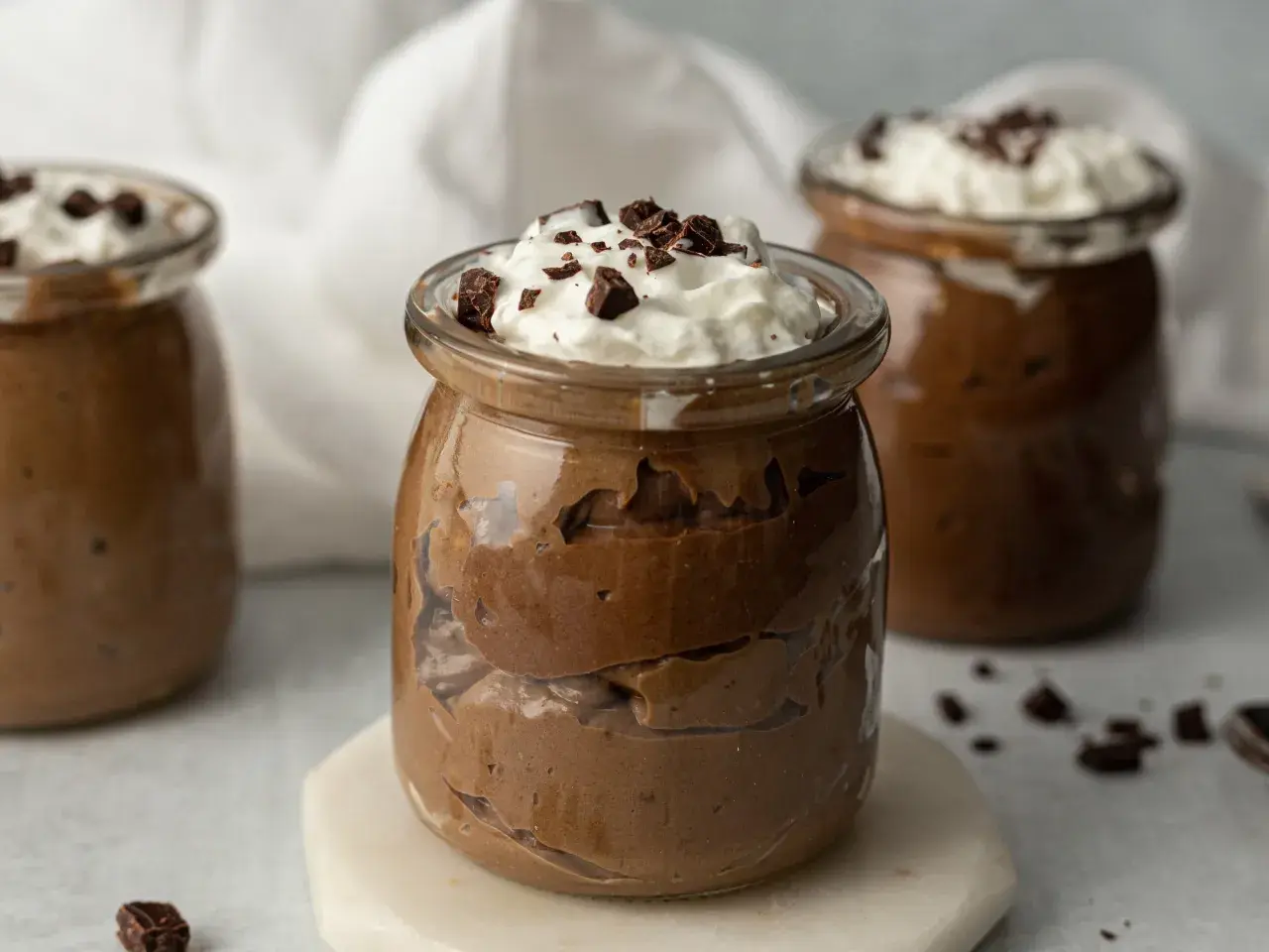 Jak zrobić pudding proteinowy: czekoladowy deser w słoiczku, udekorowany bitą śmietaną i kawałkami czekolady.