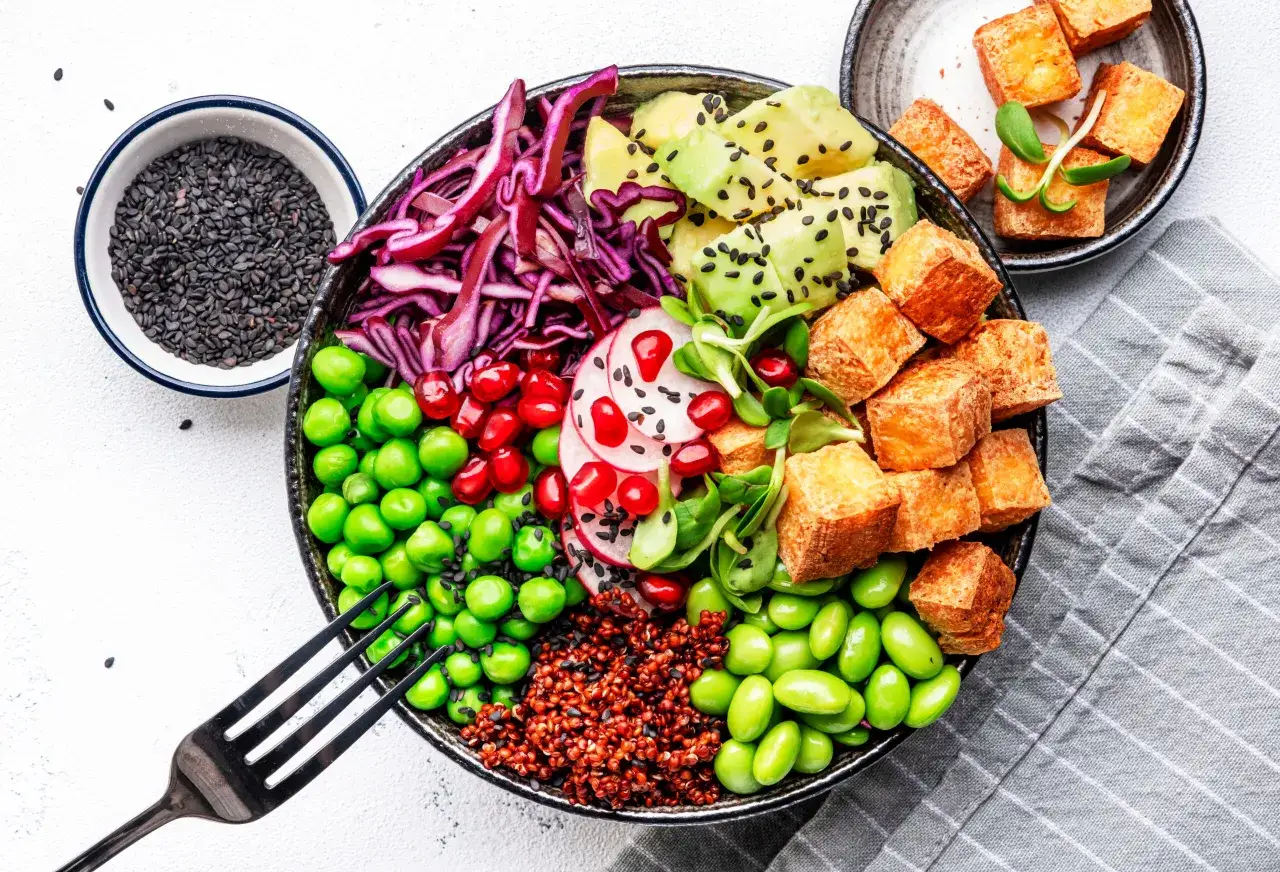 Kolorowa miska pełna zdrowia: komosa ryżowa, edamame, groszek, czerwona kapusta, awokado, tofu i nasiona czarnego sezamu. Idealna odpowiedź na pytanie: dieta wegańska co jeść.