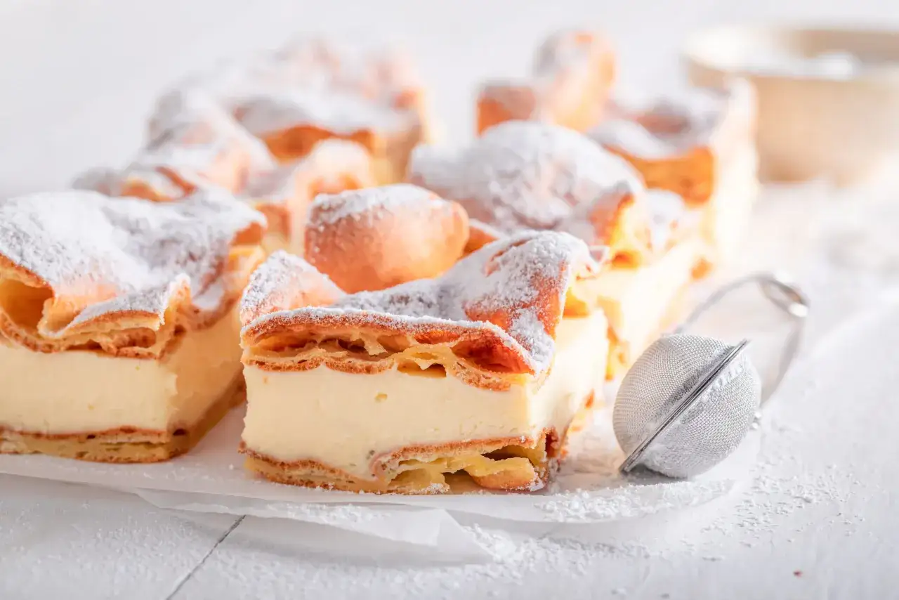 Pyszna karpatka bezglutenowa, oprószona cukrem pudrem, wygląda apetycznie. Idealna na deser, gdy szukasz przepisu bez glutenu.