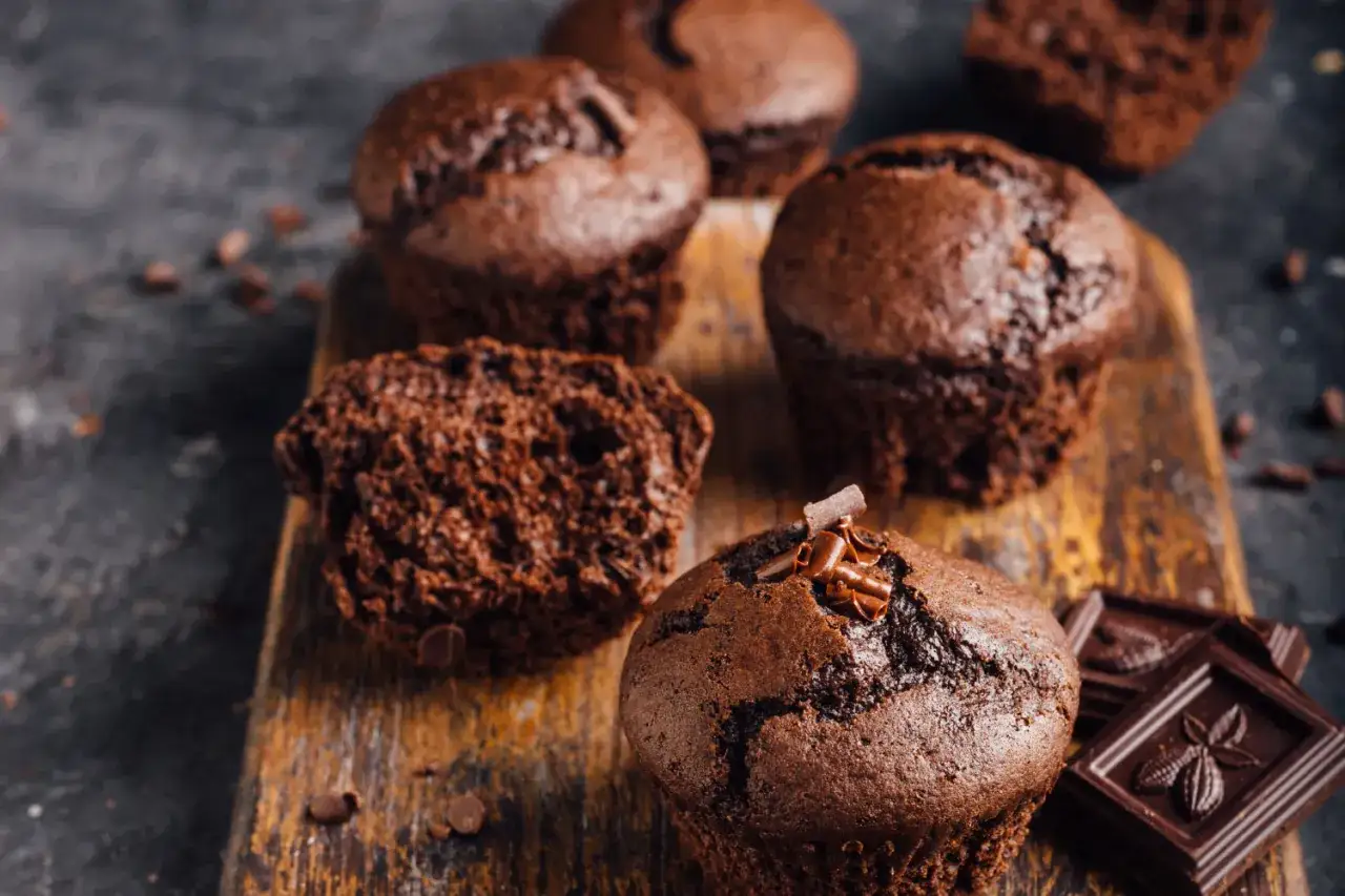 Pyszne babeczki bezglutenowe przepis na czekoladowe muffinki. Jedna przekrojona, ozdobiona wiórkami czekolady.