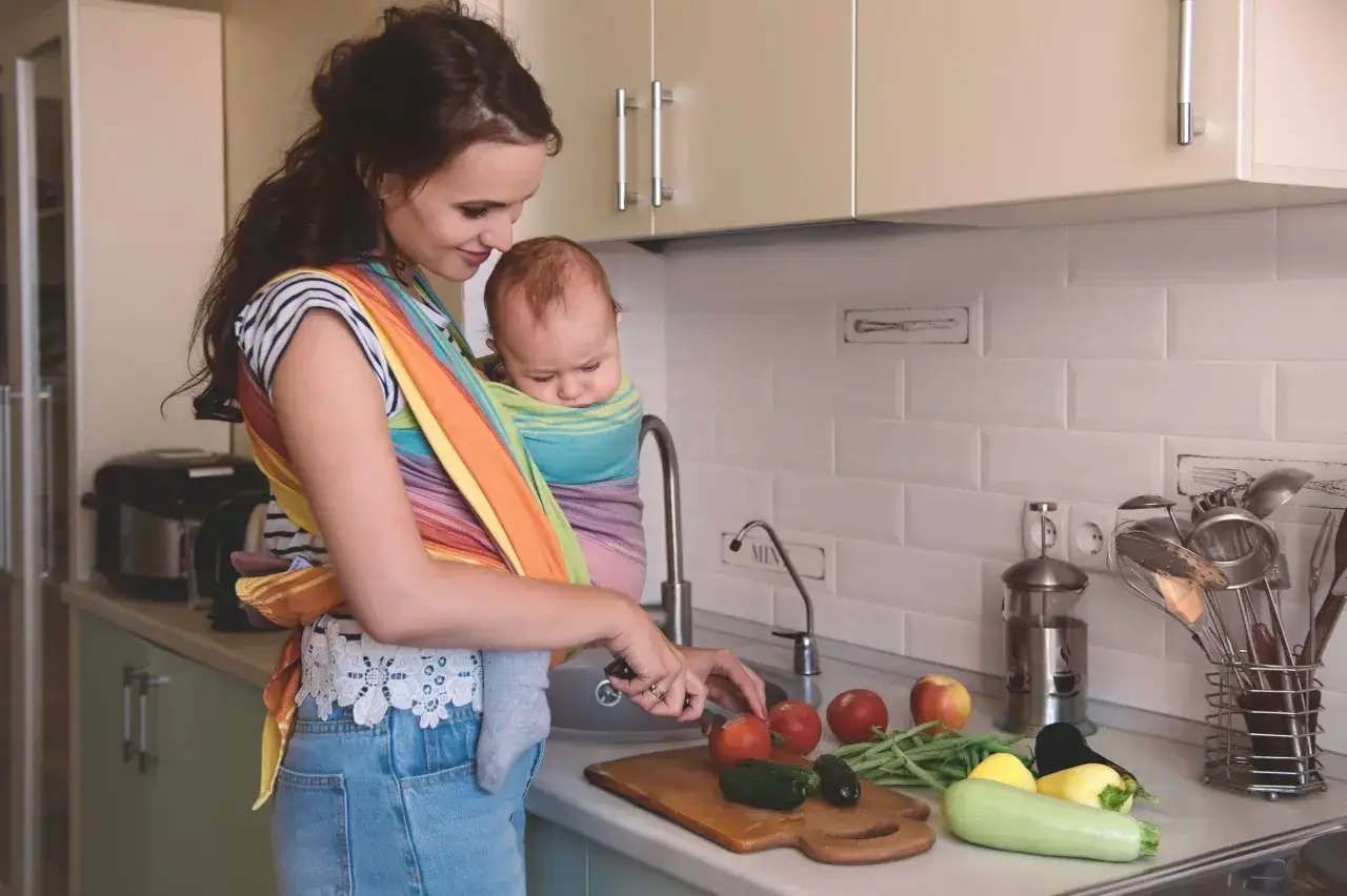 Kobieta z dzieckiem w chuście przygotowuje warzywa. Czy mleko matki jest wegańskie? To pytanie, na kt&oacute;re odpowiedź jest oczywista, gdy patrzymy na naturę.