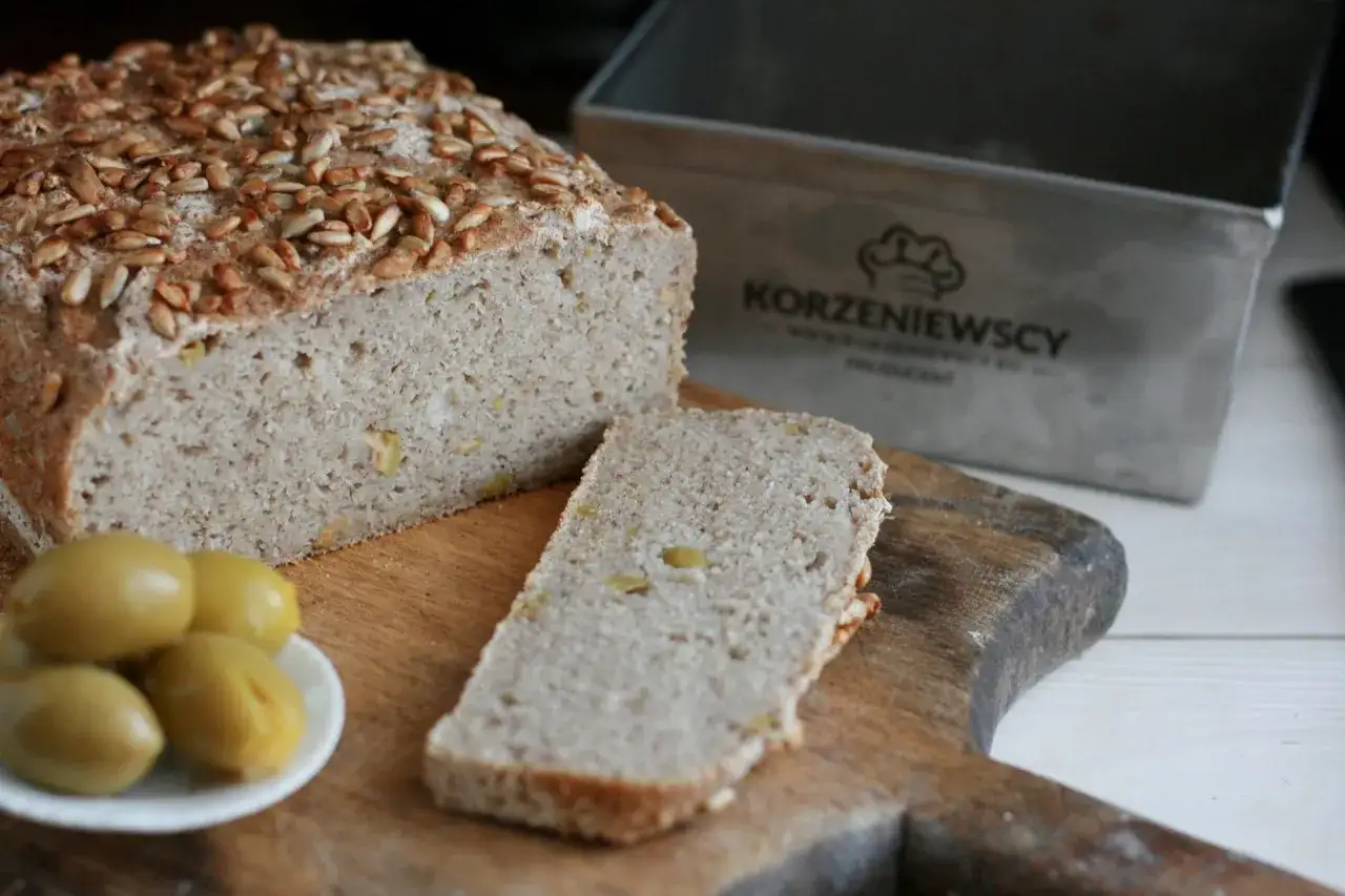 Chleb gryczany bezglutenowy, posypany słonecznikiem, z oliwkami i formą do pieczenia w tle. Idealny przepis na zdrowe śniadanie.