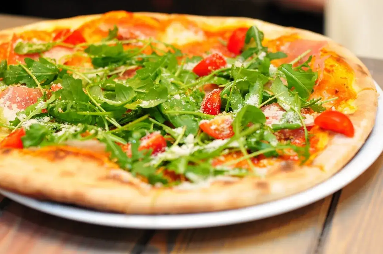 Pyszna pizza wegetariańska z rukolą i pomidorkami. Zastanawiasz się, ile kalorii ma pizza wegetariańska?