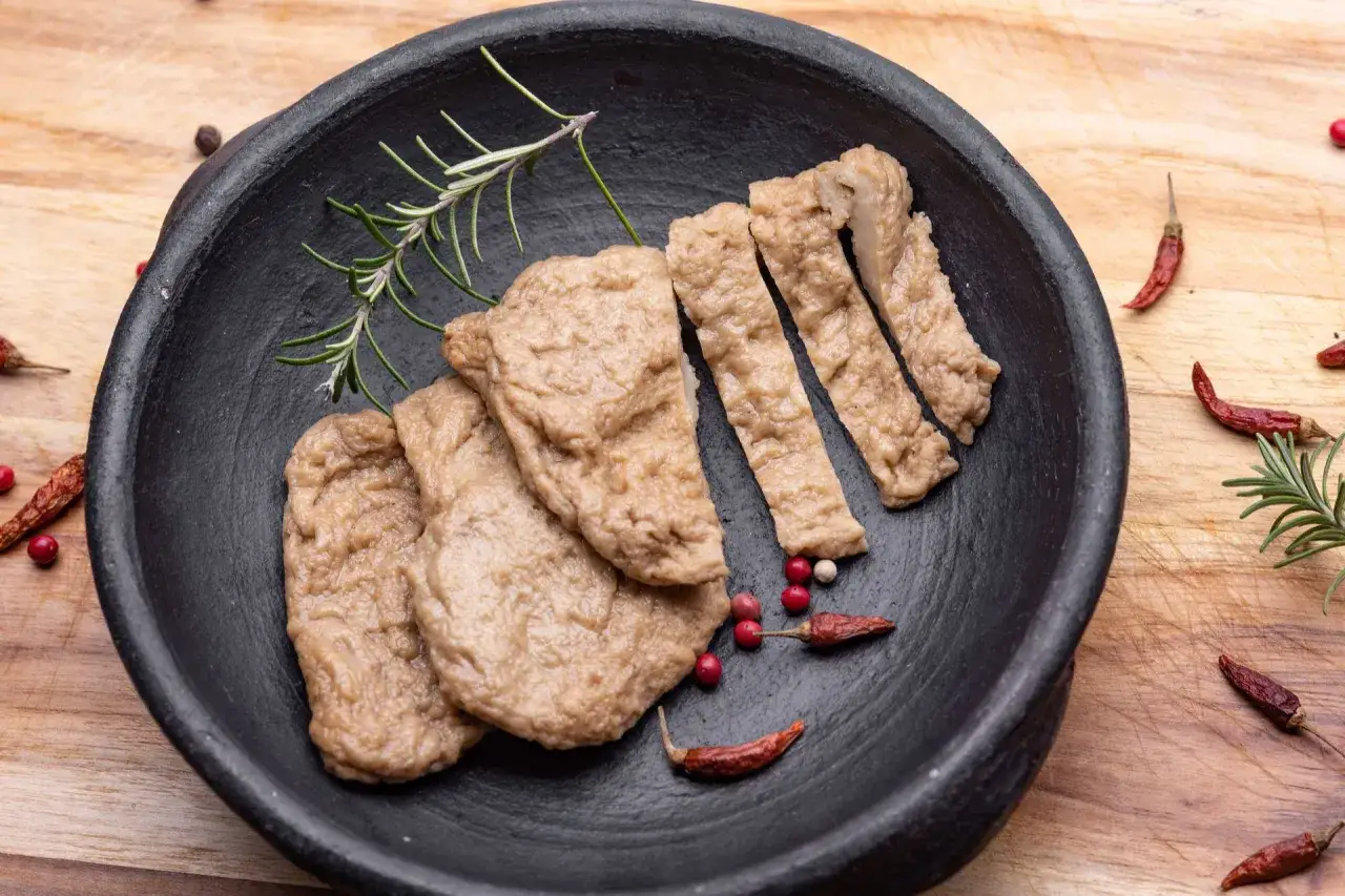 Gotowe wegańskie mięso w czarnej misie, pokrojone w paski, z rozmarynem i papryczkami chili. Idealne, by dowiedzieć się, jak zrobić wegańskie mięso.