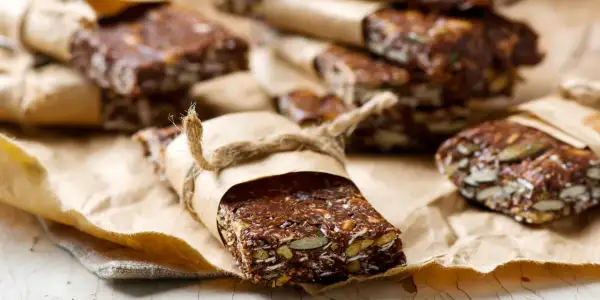 Domowe batony proteinowe z nasionami i bakaliami, zawinięte w papier i przewiązane sznurkiem. Idealne, gdy zastanawiasz się, jakie batony proteinowe wybrać.