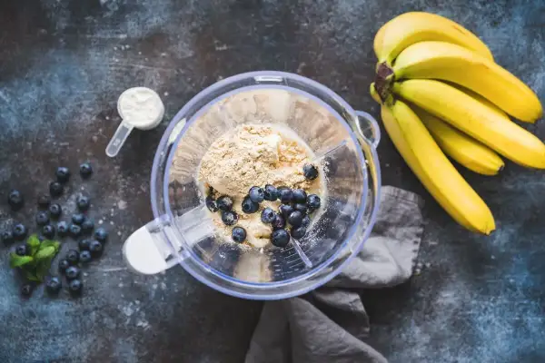 Jak zrobić shake proteinowy: banany, borówki, odżywka białkowa i mleko w blenderze.
